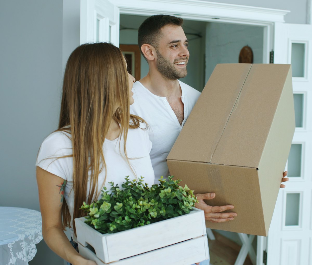A couple carrying moving boxes into their bright new home